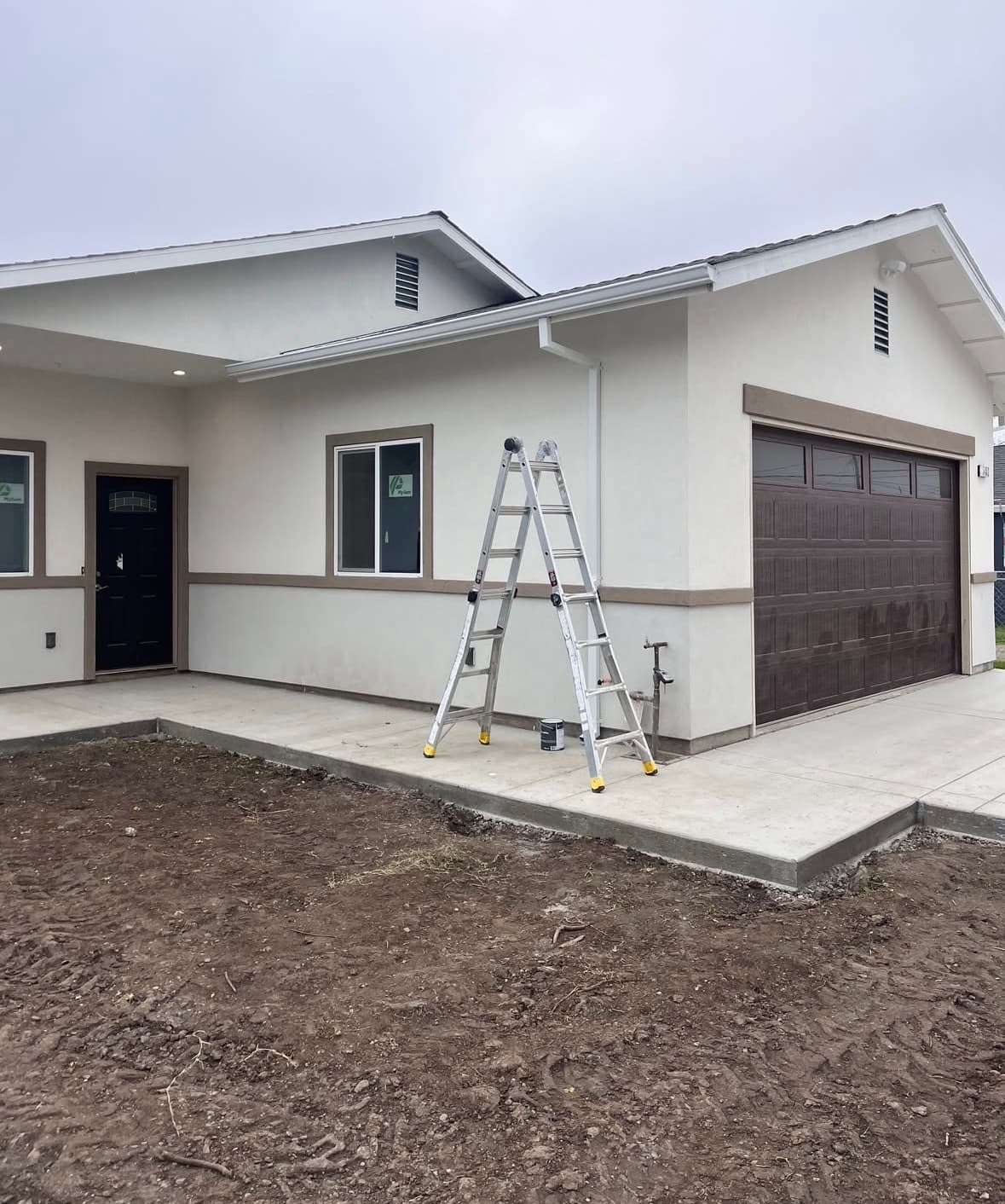 Newly painted house with dark garage, ladder, concrete path, and dirt foreground.