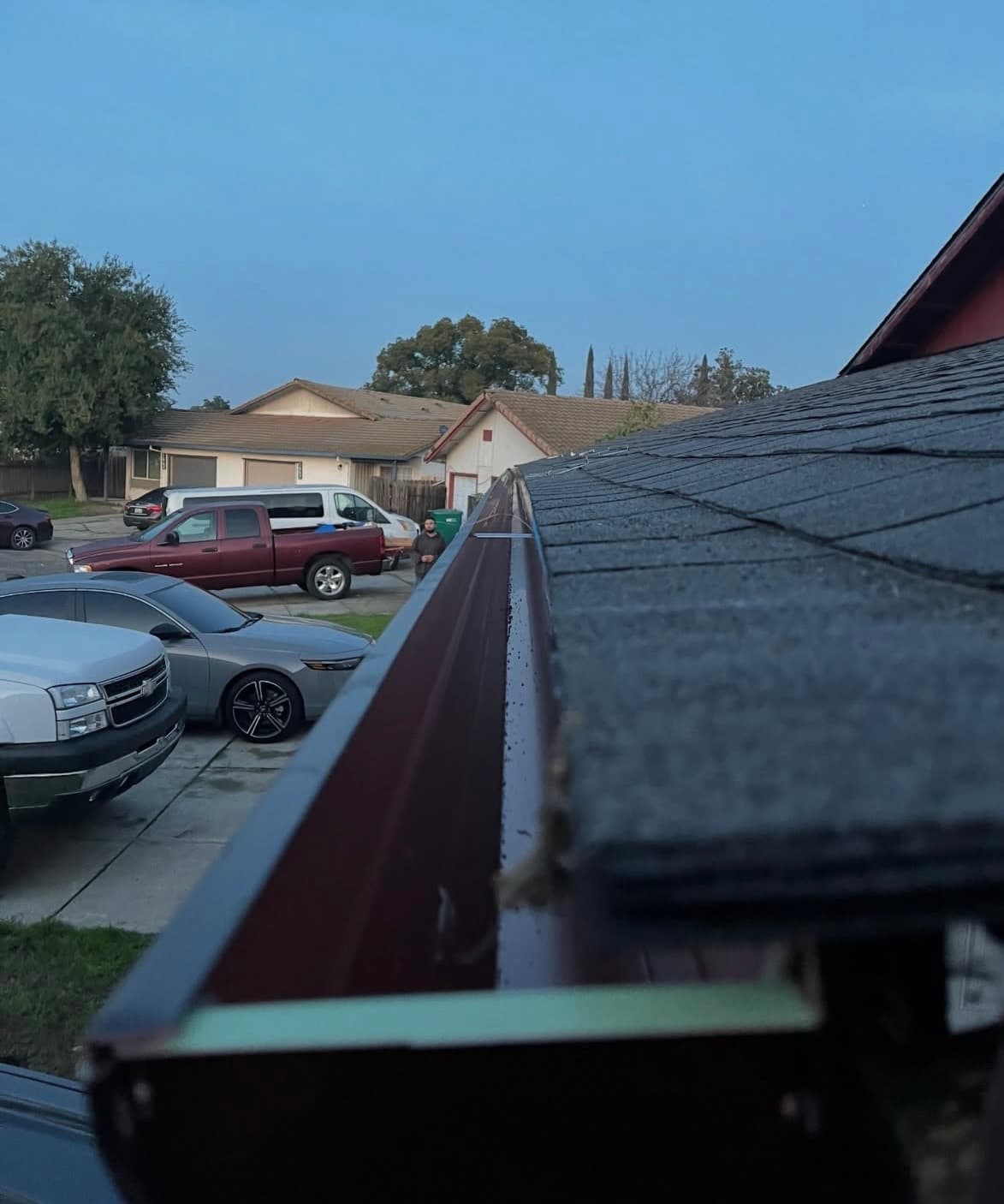Close-up of a red roof gutter, with parked cars and houses under a blue sky.