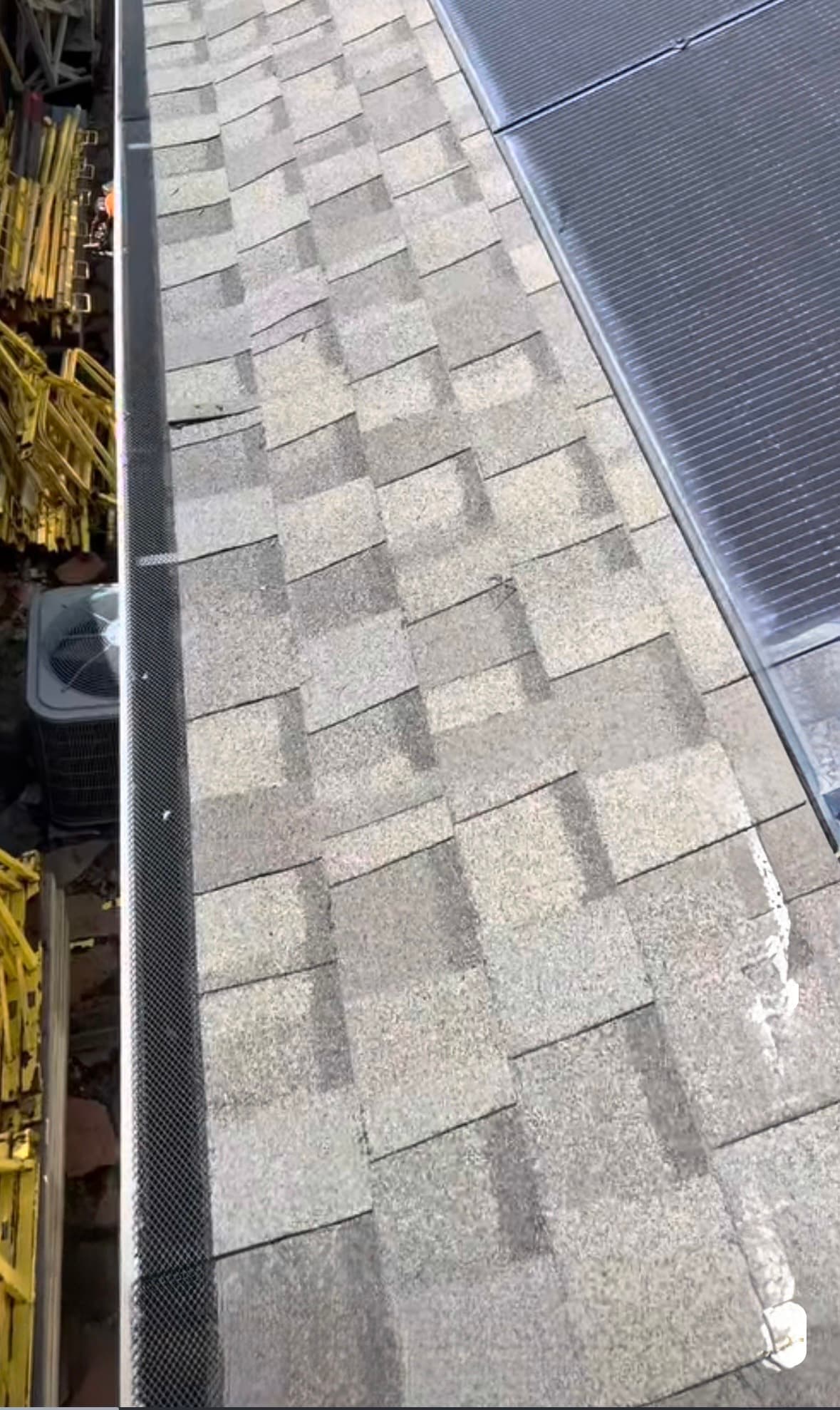 Stained asphalt shingle roof with gutter guard, solar panels, and equipment below.