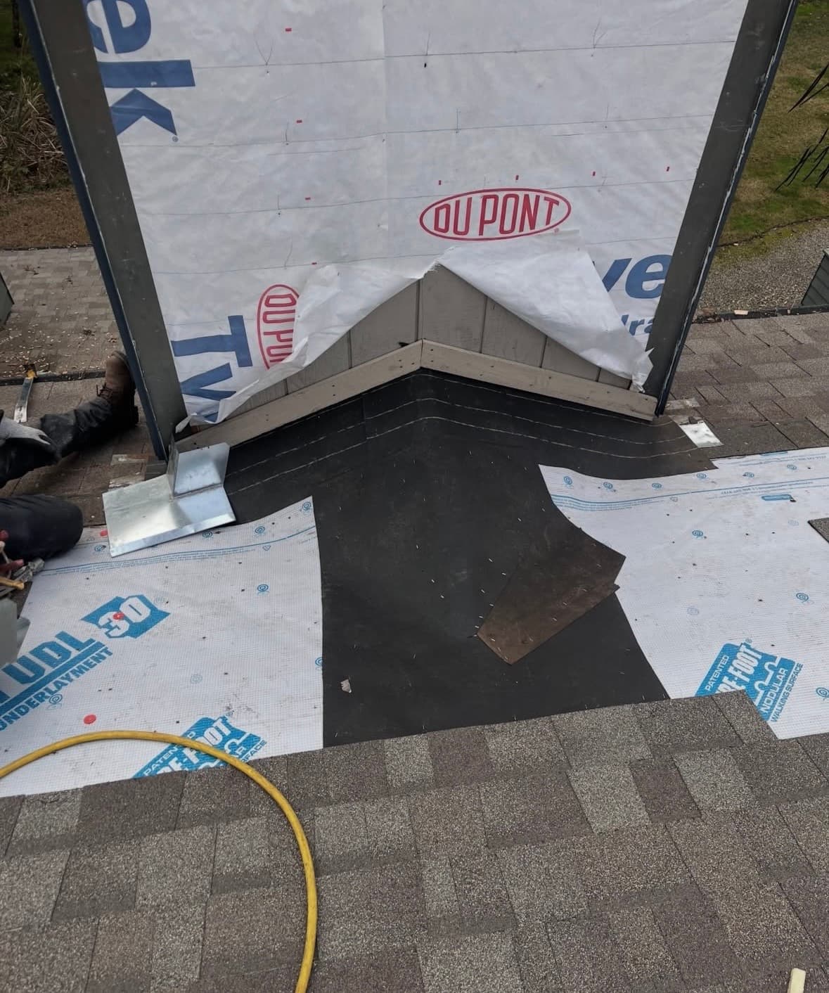 Rooftop view of new shingles, underlayment, and Tyvek wrap around a dormer base.